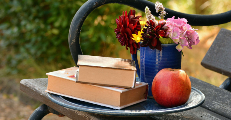 Panchina con sopra due libri, un vaso di fiori e una mela