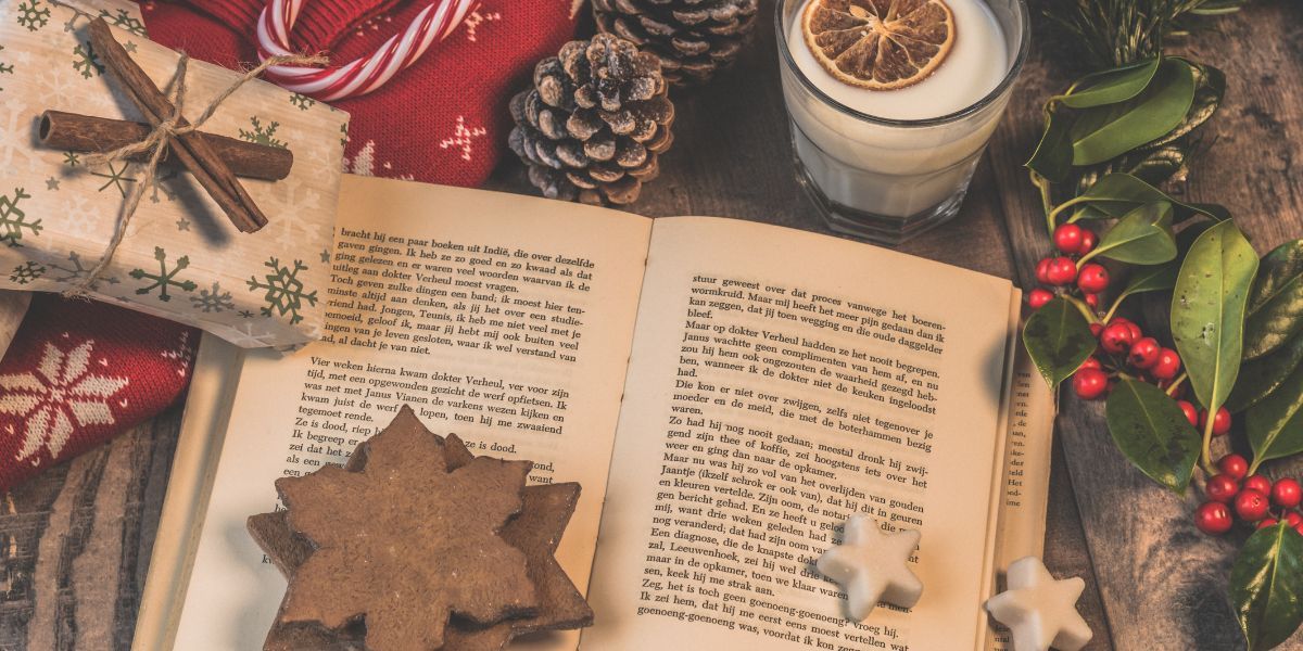 libro aperto con biscotti sopra a forma di stella e intorno pacchetti di natale e candela