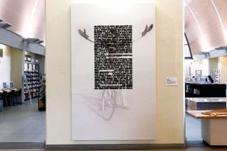 tela bianca con parole cancellate e sullo sfondo foto di Malaparte su bicicletta con braccia sollevate al cielo