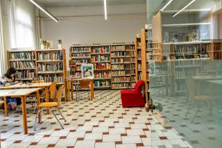 Vista della sala lettura con scaffali e libri, tavoli e sedie, e una ragazza che studia.