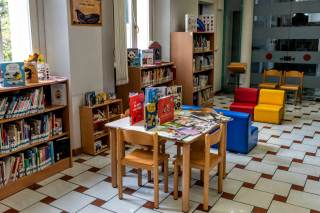 Veduta sala con scaffali con libri per l\'infanzia, tavolini e sedioline a misura di bambino.