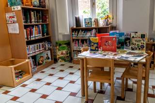 Tavolo con libri appoggiati sopra e sedioline a misura di bambino, scaffali con libri per l\'infanzia.